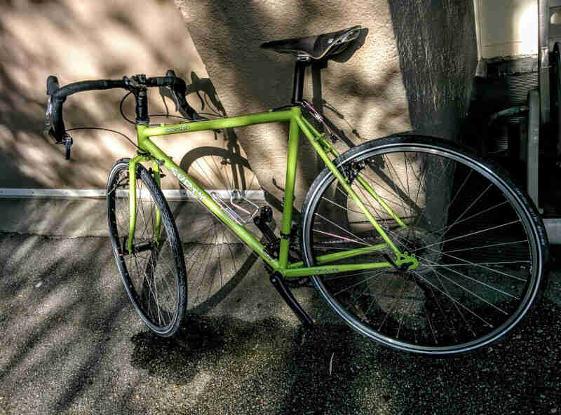 Left side view of a lime green Surly bike, leaning against a tan stone wall of a building