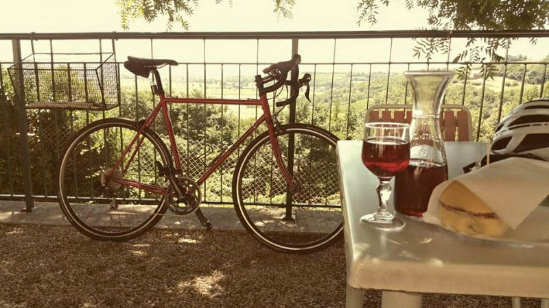Right side view of a red Surly bike, leaning on the guardrail on a balcony with a table and trees in the background