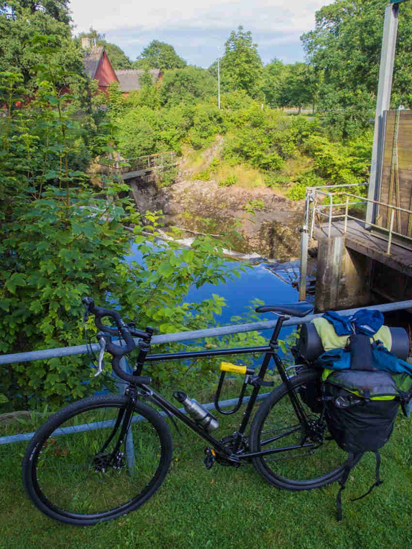 Downward, left side view of a black Surly Straggler bike, parked against a railing, with a river below in the background