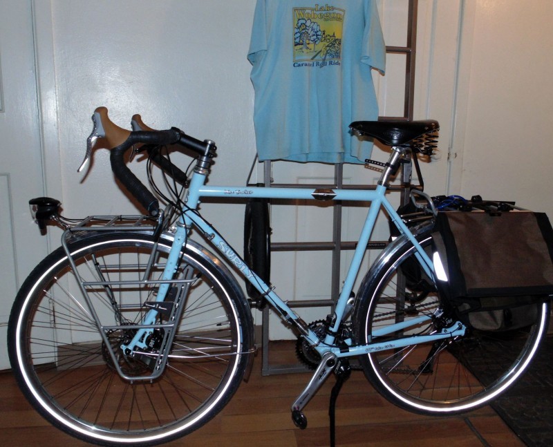 Left side view of a light blue Surly Disc Trucker bike, parked in a room with a wood floor and white walls