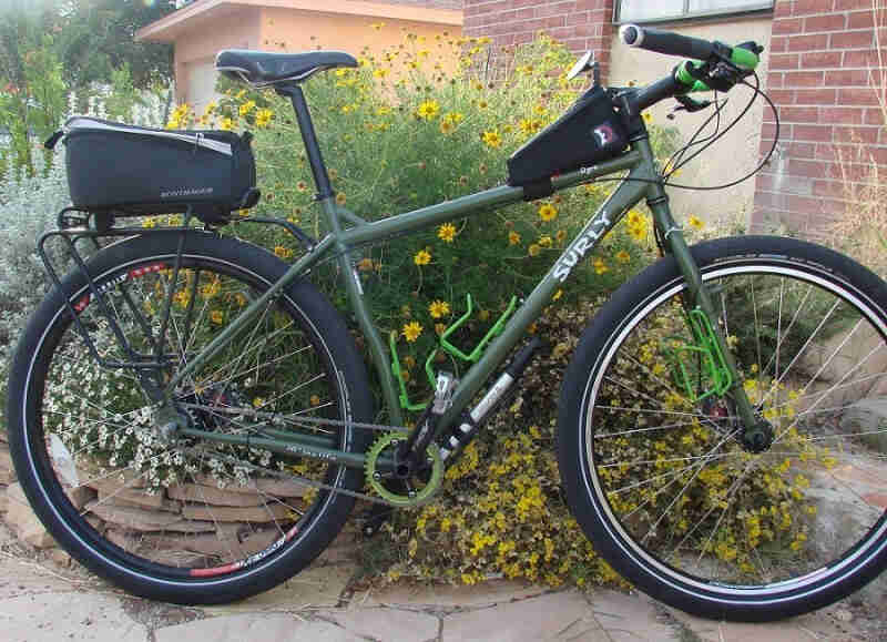 Right side view of an olive drab Surly Ogre bike with rear pack, leaning on flowery landscaping next to a house