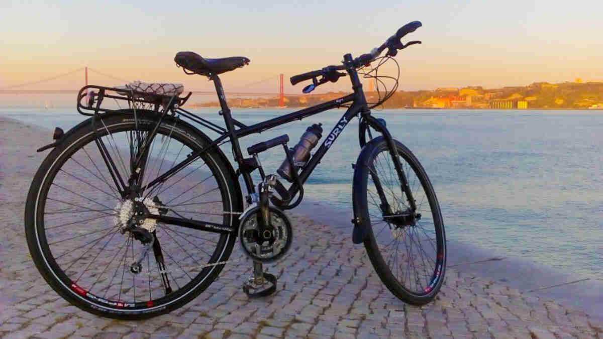 Right side view of a black Surly Ogre bike, parked on a brick courtyard along a river, with a city in the background