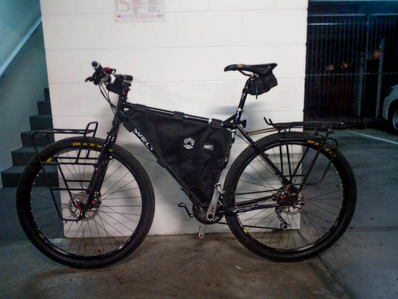 Left side view of a black Surly Ogre bike with a frame bag and gear racks, leaning on a wall in a parking garage