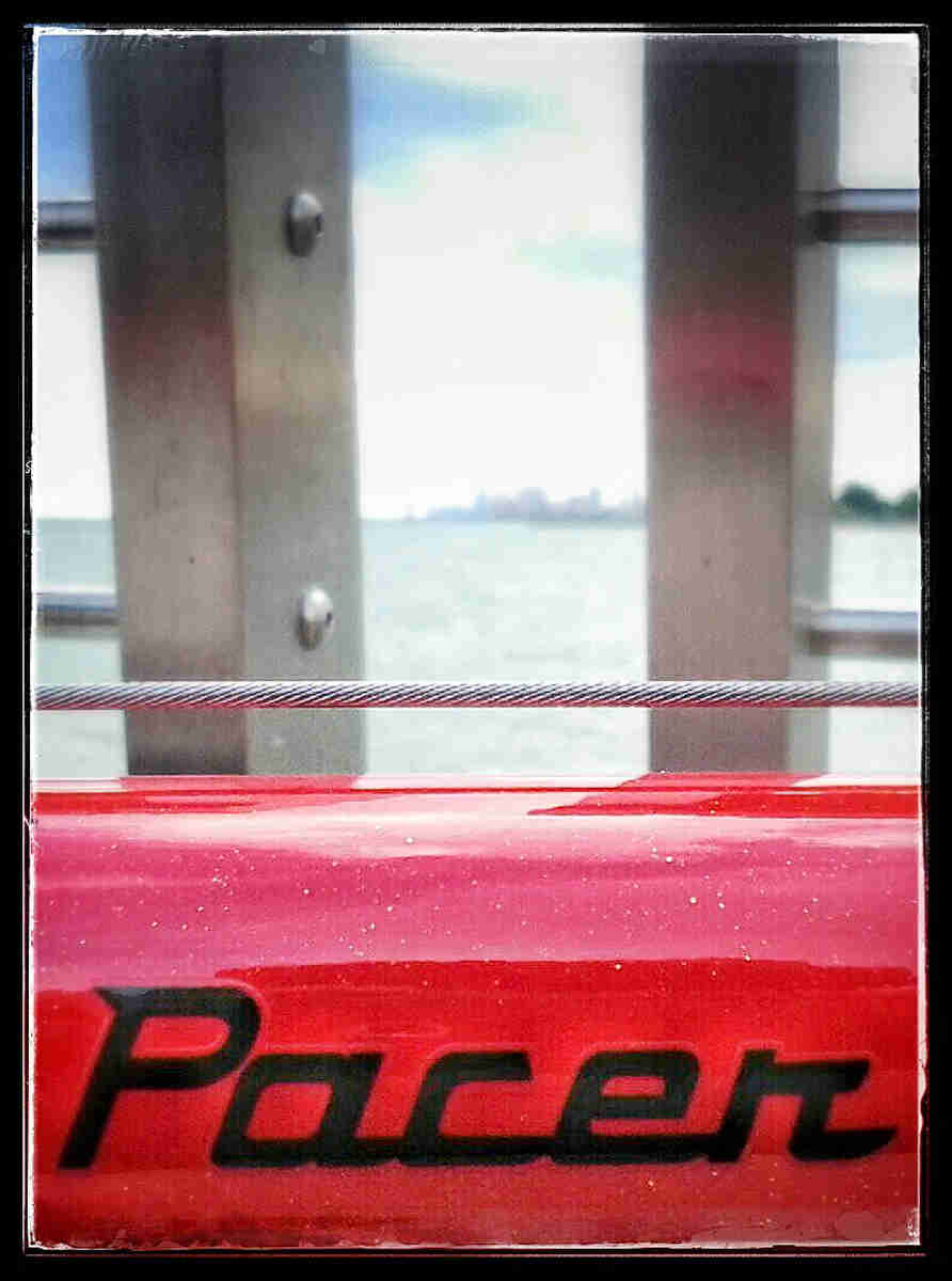 Zoomed in, close up view of a Pacer sticker, on the top tube of a red Surly bike, with a cable above 