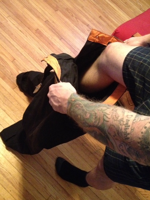 Downward view of a person pulling on a pair of black Surly pants, with a wood floor below