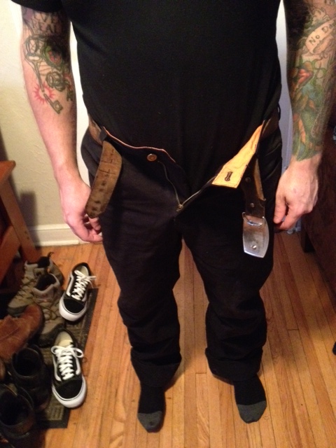 Front, chest down view of a person wearing black Surly pants in a room with wood floors