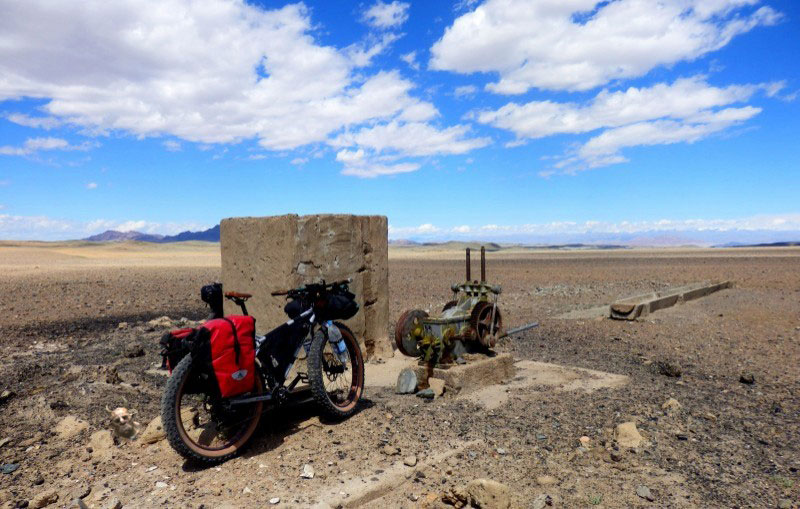 Right side view of a Surly Pugsley fat bike, loaded with gear, parked next to a well in a rocky desert