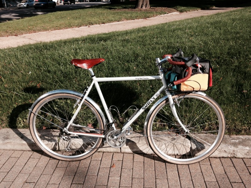 Right side view of a white Surly Long Haul Trucker bike, on a brick sidewalk with green grass behind it