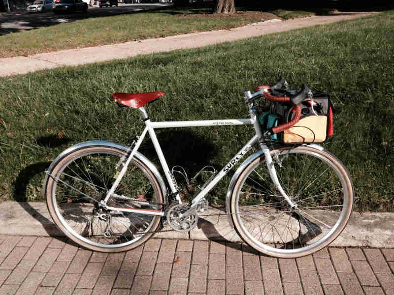 Right side view of a white Surly Long Haul Trucker bike, on a brick sidewalk with green grass behind it