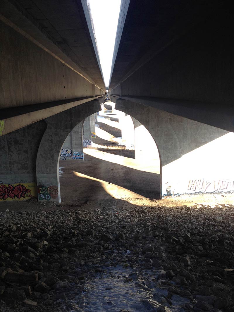 A downward view from between the decks of 2 concrete bridge overpasses that are facing straight away
