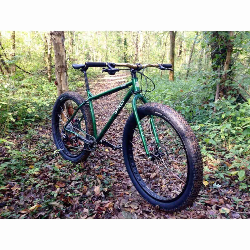 Front, right side view of a green Surly Krampus bike, parked on a leafy dirt trail in the woods