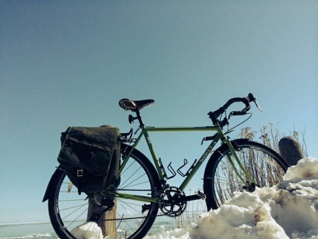 Right side view of a green Surly bike with rear saddlebags, parked in a snow bank