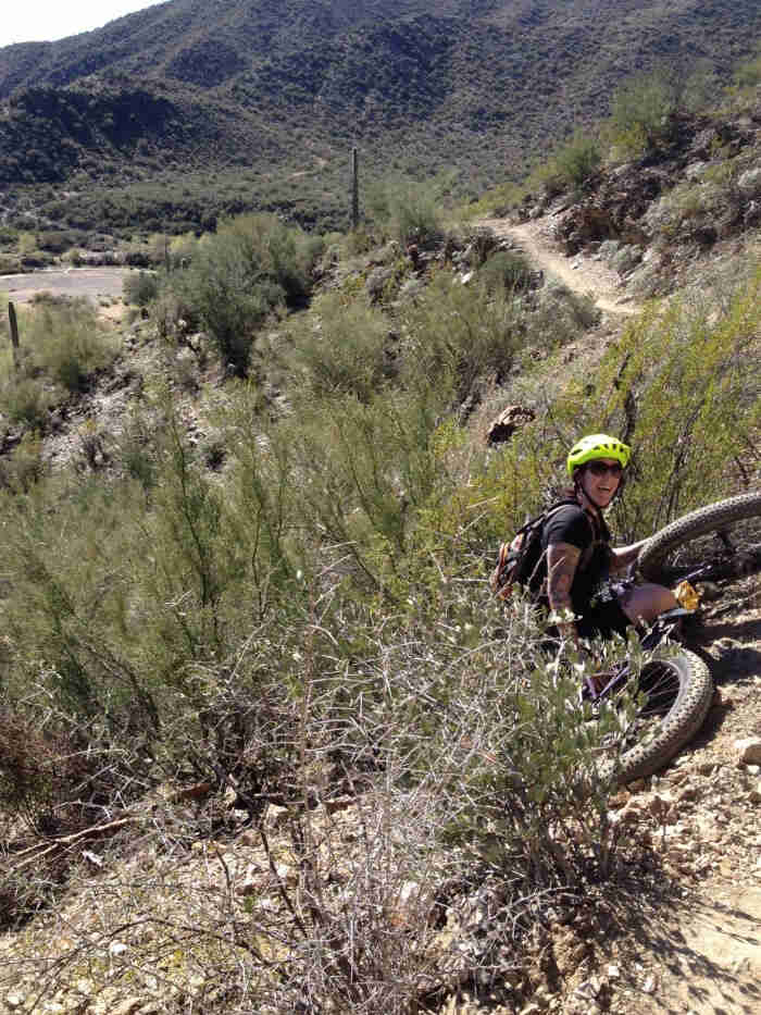 Rear view of a cyclist and their fat bike, laying in the brush on the side of a dirt trail in the desert hills