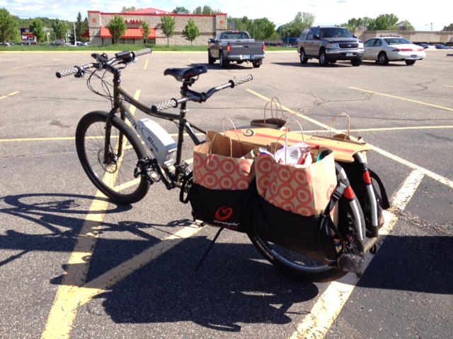 Rear, left side view of a Surly Big Dummy bike, with groceries in the rear bags, in the middle of a paved parking lot
