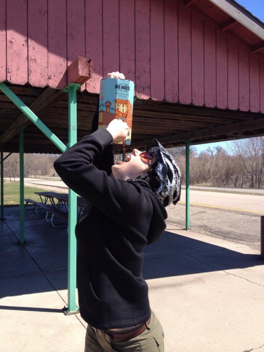 A person holding up a box of wine, dispensing it into their mouth, on the outside of a park shelter