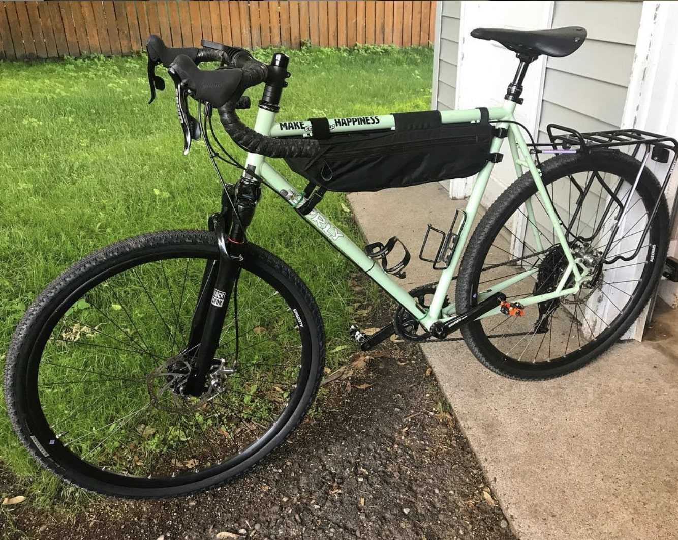 Left side of Surly Straggler bike, mint green, with rear gear rack leans on a doorway near a grassy yard with wood fence