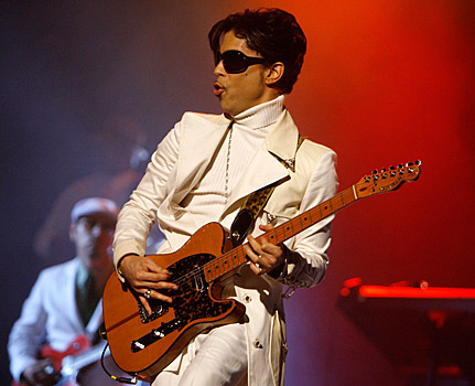 Front view of the musician, Prince, playing a guitar on stage with red lights