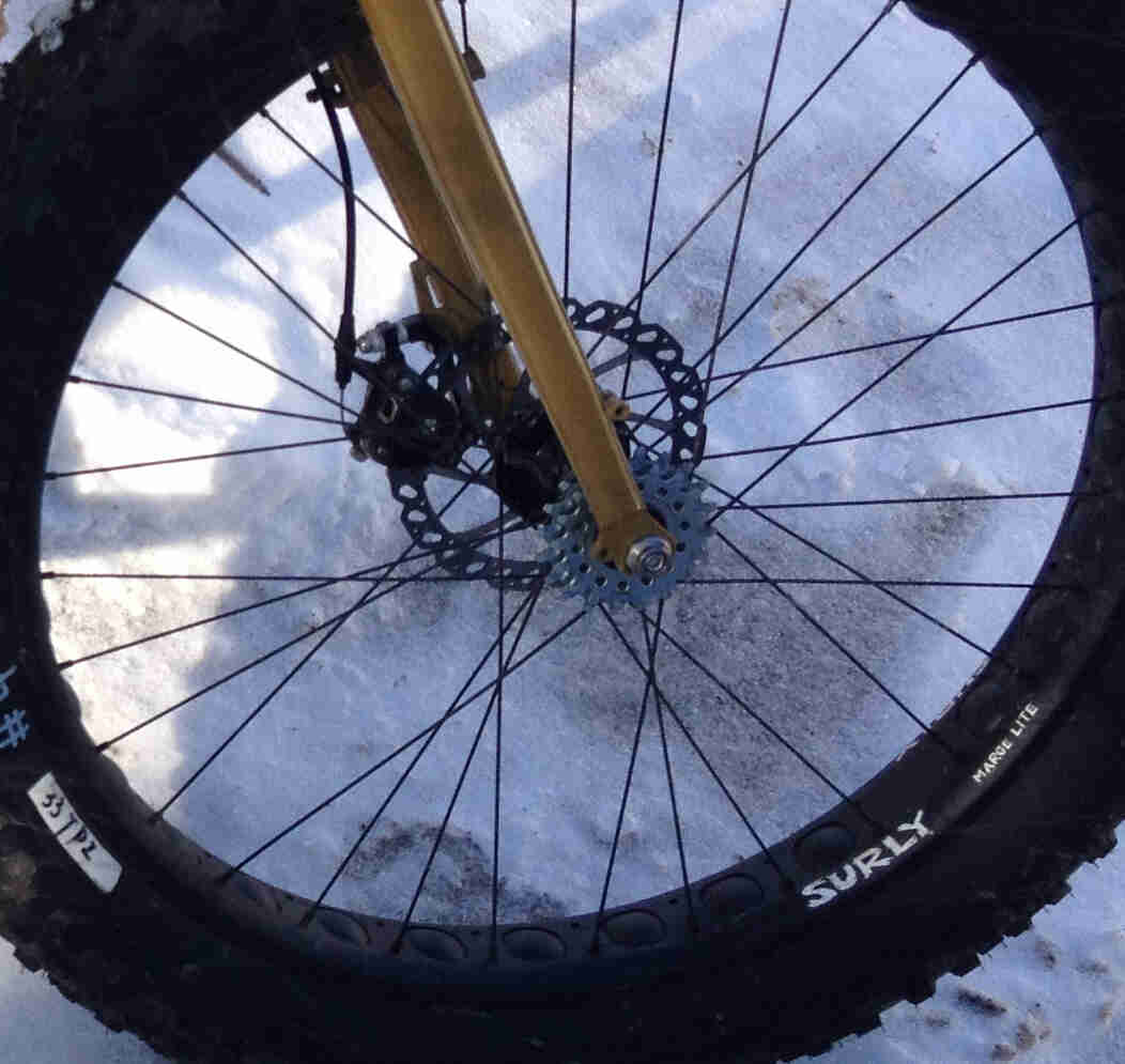 Right side view of the front wheel, with a flip-flip hub, on a mustard yellow Surly Pugsley fat bike