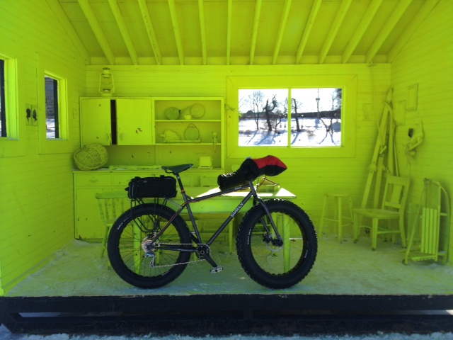 Right side view of black Surly Pugsley fat bike with a handlebar and rear pack, in a room painted fluorescent green