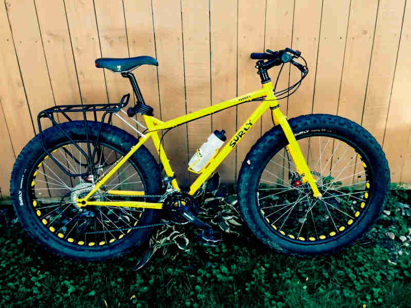 Surly Pugsley fat bike - yellow - right side view - parked in weeds alongside a wood fence