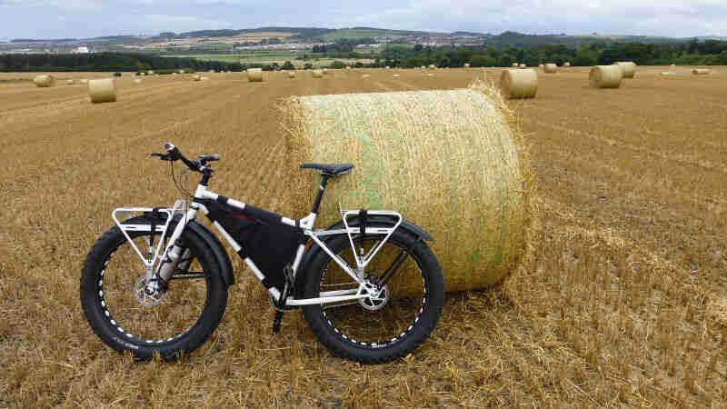 Left side view of a Surly Pugsley fat bike, white, in a hayfield with rolls of hay scattered around