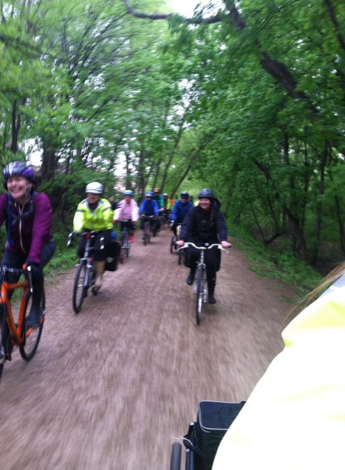 Front view of a group of cyclists riding down a gravel road in a rainy day in the green woods