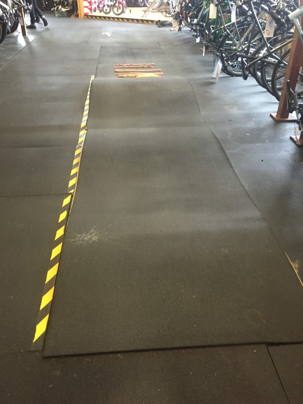 A black demo course mat, on the floor of a bike shop