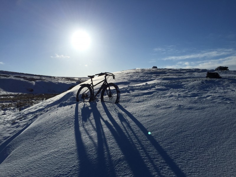 Right side view of a Surly ECR bike, standing in the middle of a deep snow covered hill, with the sun shining above