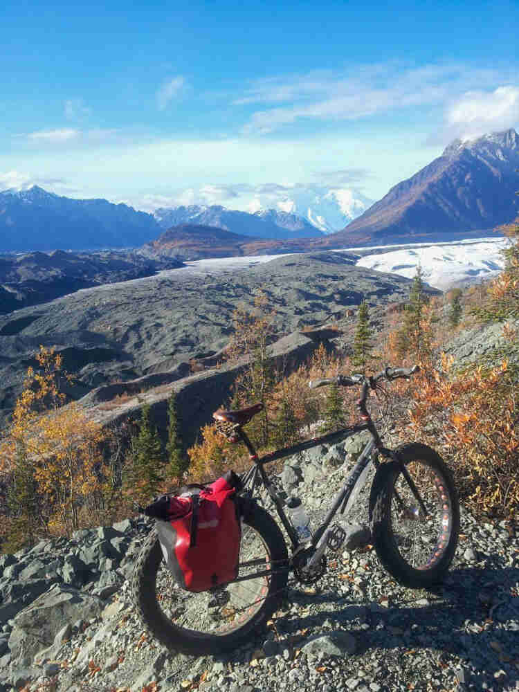 Right side view of a Surly fat bike, parked on a rocky hilltop, with a glacier and mountains in the background