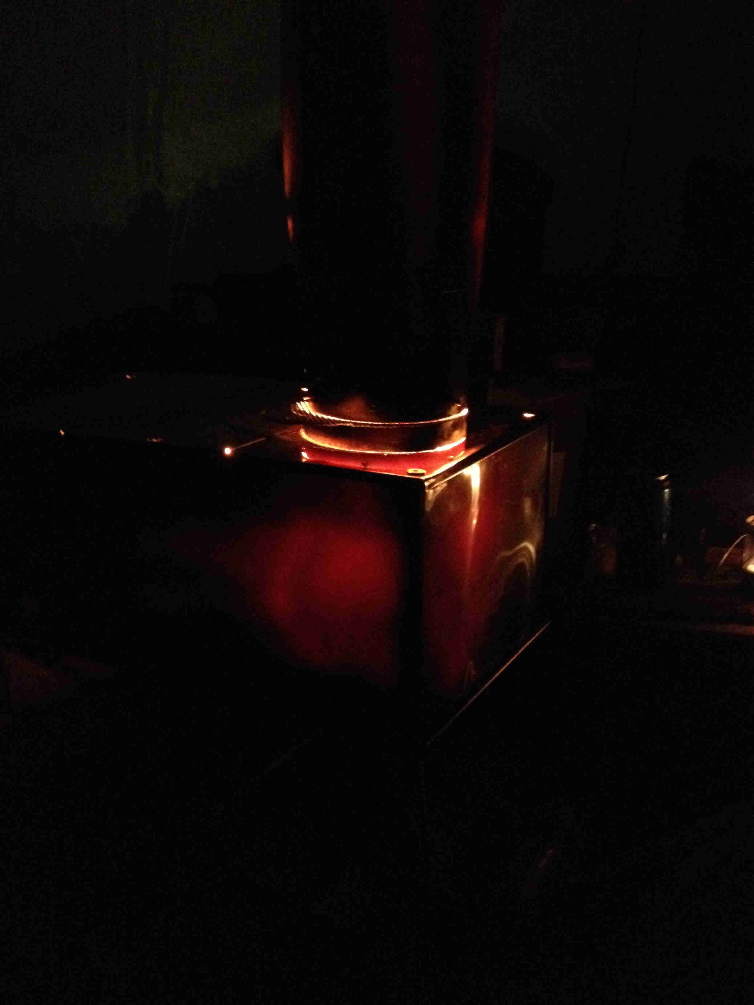 Dark, nighttime view of a stainless steel portable stove with a glowing burner