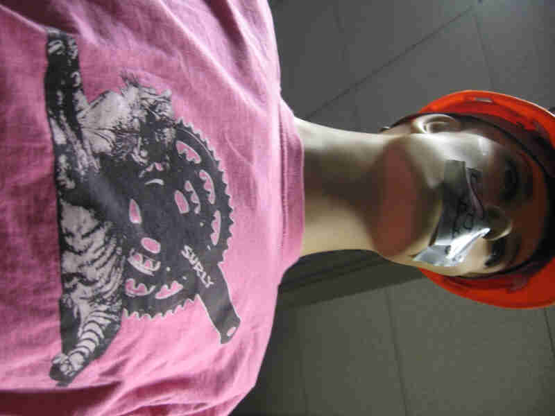 Upward, waist up view of mannequin, wearing a pink Surly Bikes t-shirt with graphic of a bike crank and a tiger