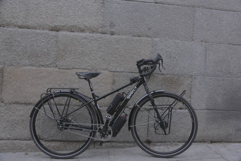 Right side view of a black Surly bike, parked on a sidewalk, leaning against a stone block wall