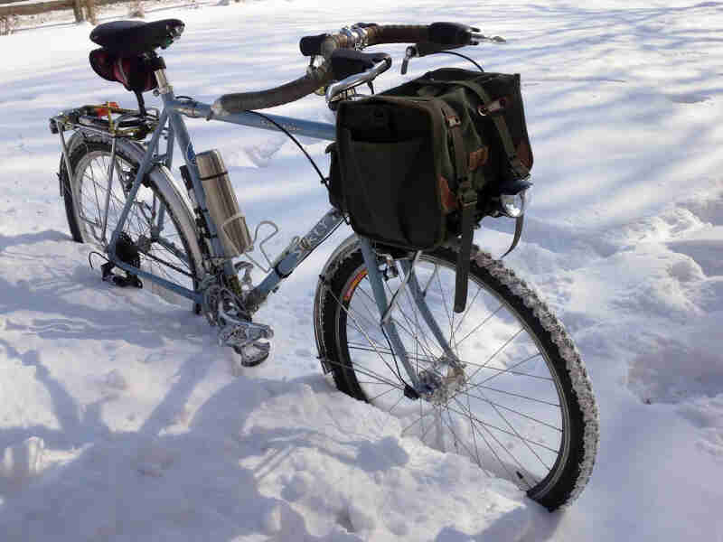 Front right side view of a Surly bike, light blue, with a front pack, parked in a deep snow-covered field
