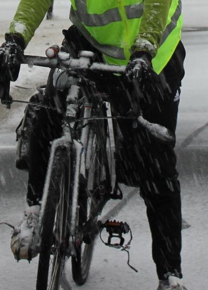 Front view of a Surly bike, with a cyclist shown from the chest down, riding on a snow covered street