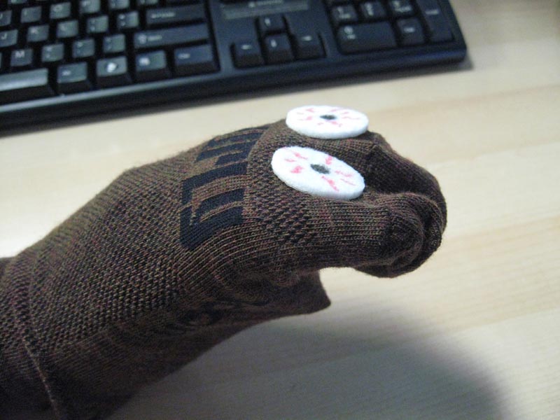 Downward view of a person's hand, inside of a brown sock puppet, above a desk with a computer keyboard on it