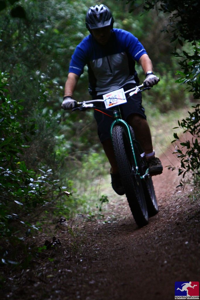 Front view of a cyclist, riding a green Surly Krampus bike down a dirt trail with bushes on the sides