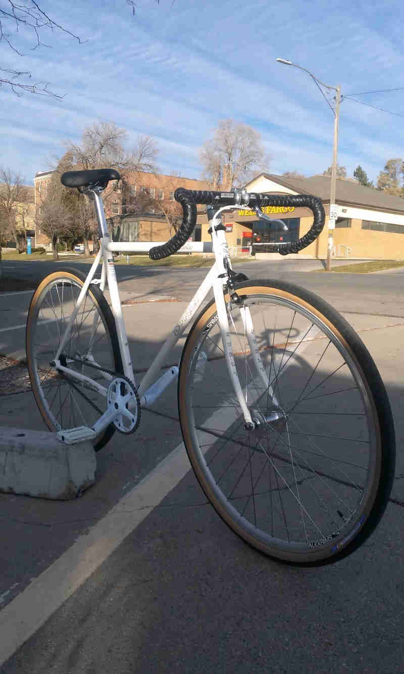 Right side view of a white Surly Steamroller bike, in a roadside parking spot, with a Wells Fargo building in background