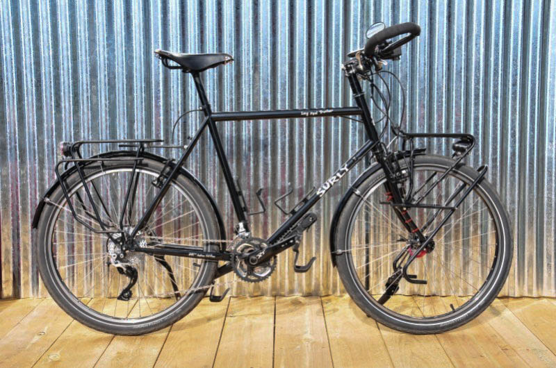 Right profile of a Surly Long Haul Trucker bike, black, in front of a corrugated steel wall