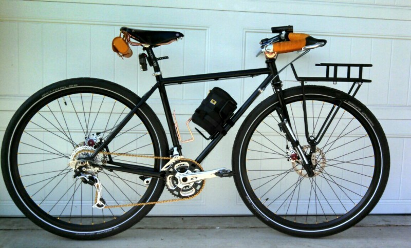 Right side view of a black Surly Straggler bike, leaning on the outside of a closed, white garage door