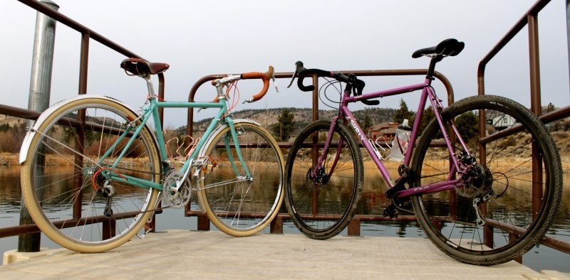 Rear view of two Surly Straggler bikes angled inward with their front wheels touching, on a dock facing a pond