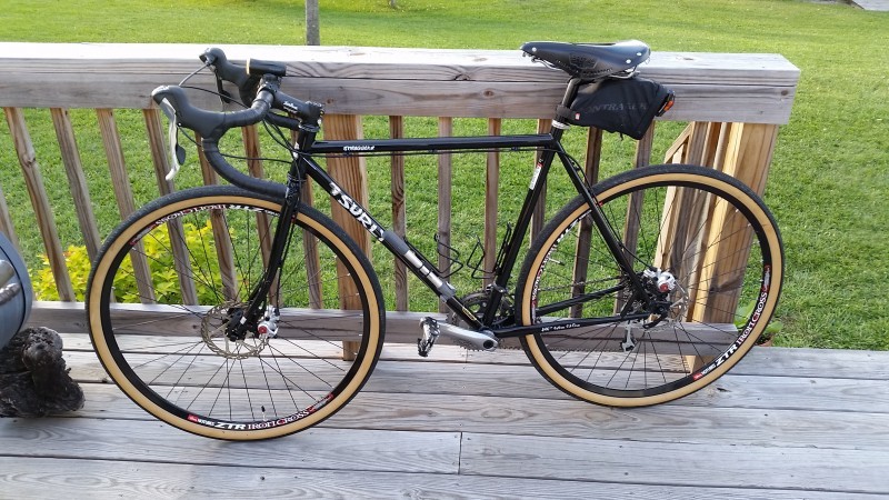 Left side view of a black Surly Straggler bike, leaning on the handrail of a deck, with a green grassy yard below