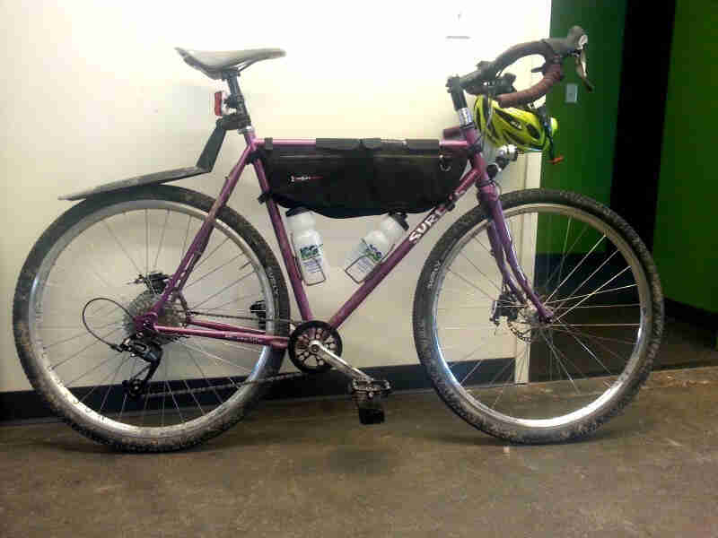 Right side view of a raspberry color Surly Straggler,  parked in a hallway against a white wall