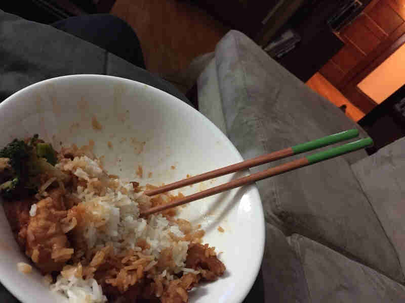 Downward view of a bowl with rice and chopsticks inside, in a room of a house 