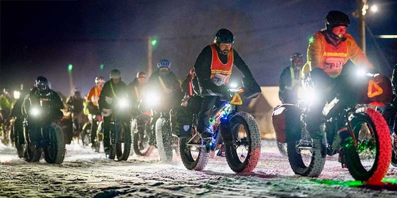 Alex and Ian riding Surly Moonlander fat bikes out at 2025 Arrowhead 135 start in dark with other racers