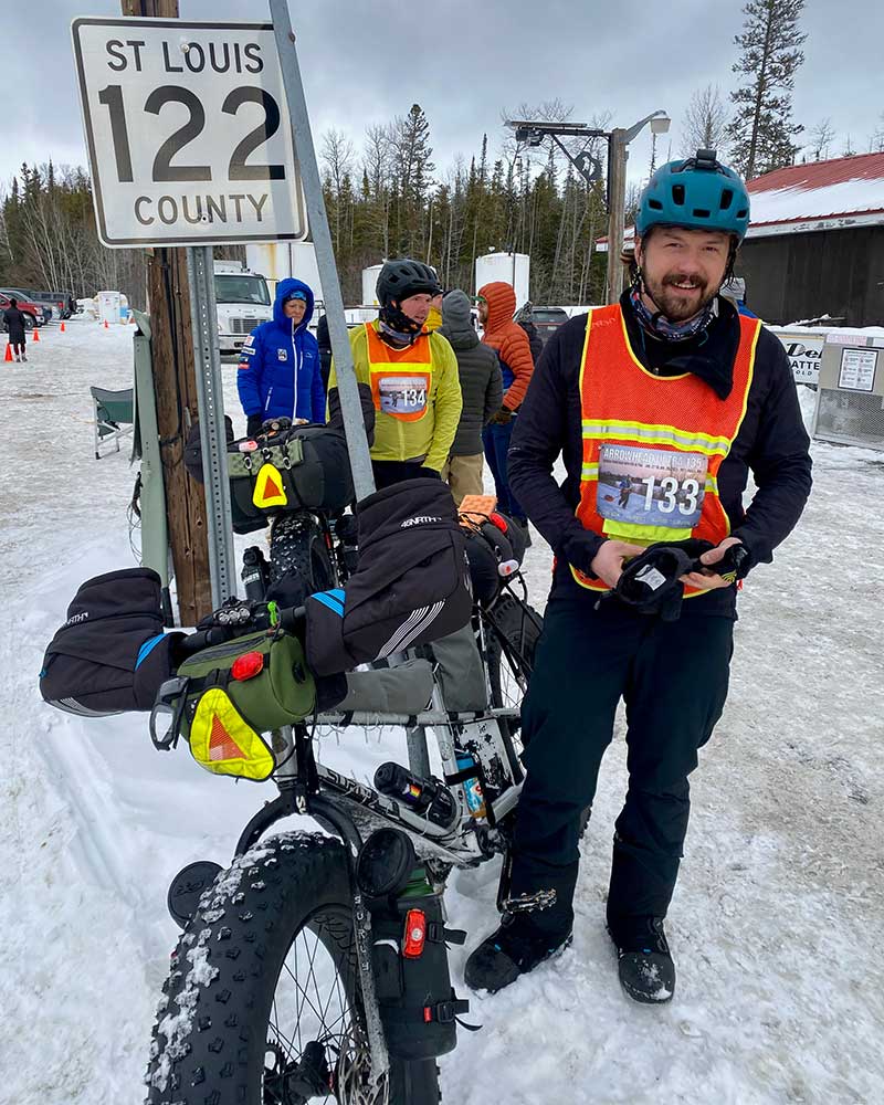 Alex smiling outside checkpoint with Ian loaded Surly Moonlander fat bikes parked