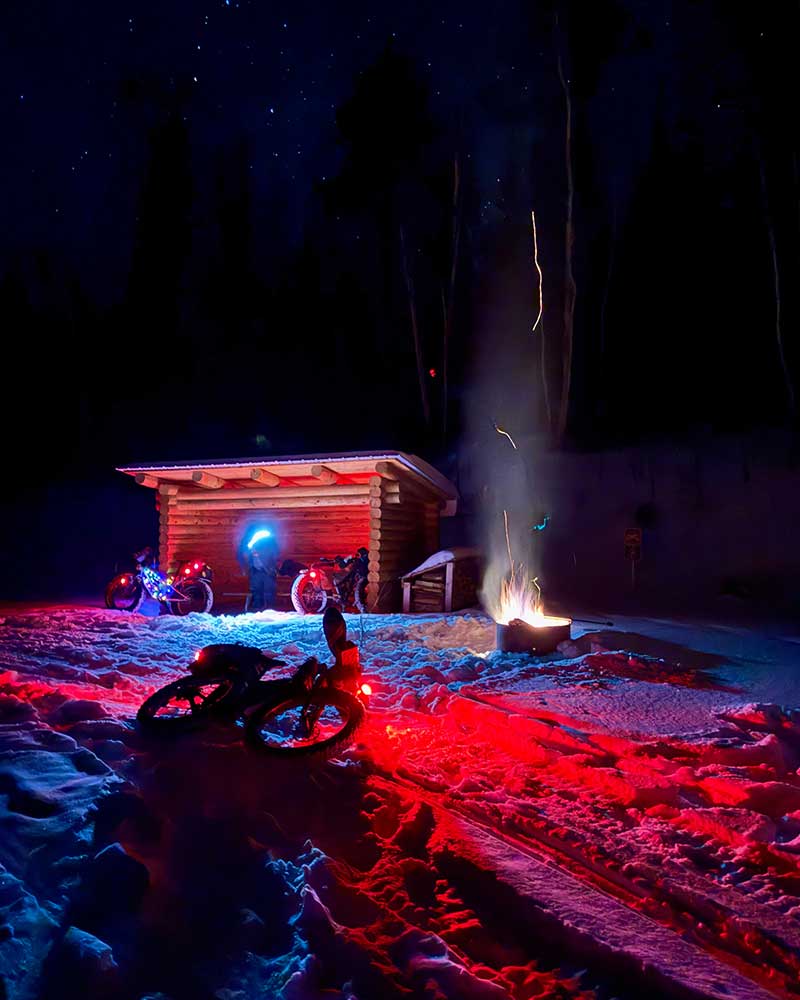 Arrowhead 135 fat bike racers at wayside rest stop at night with camp fire going