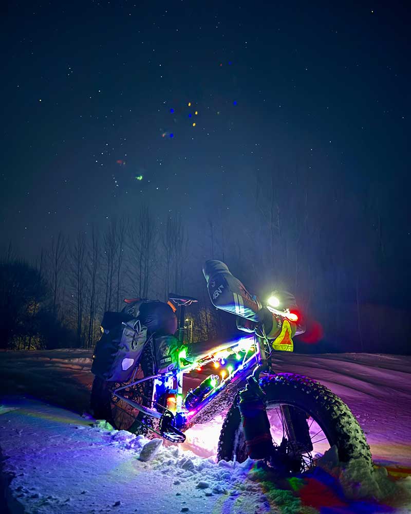 Loaded Surly Moonlande fat bike parked beside trail in snow with xmas lights on at night