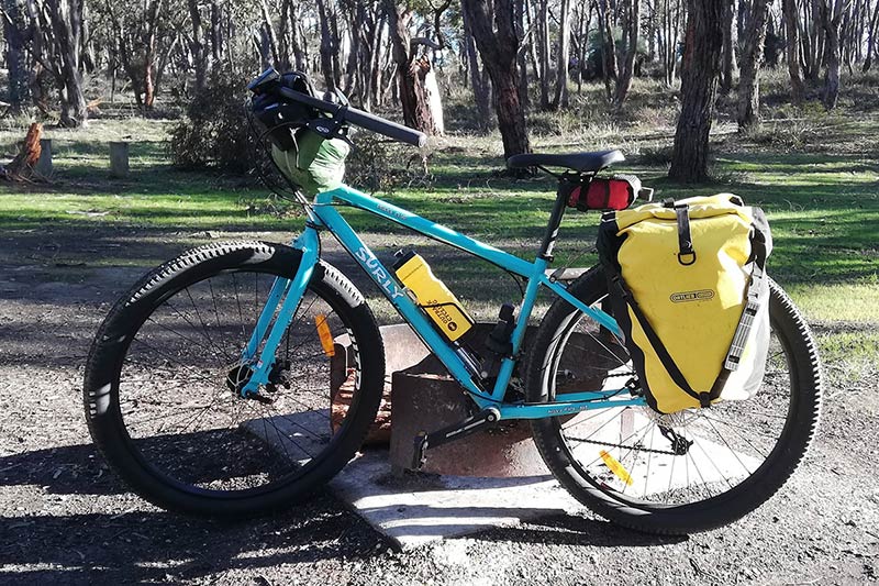 Light blue Surly Bridge Club bike leaning against campfire ring loaded for touring