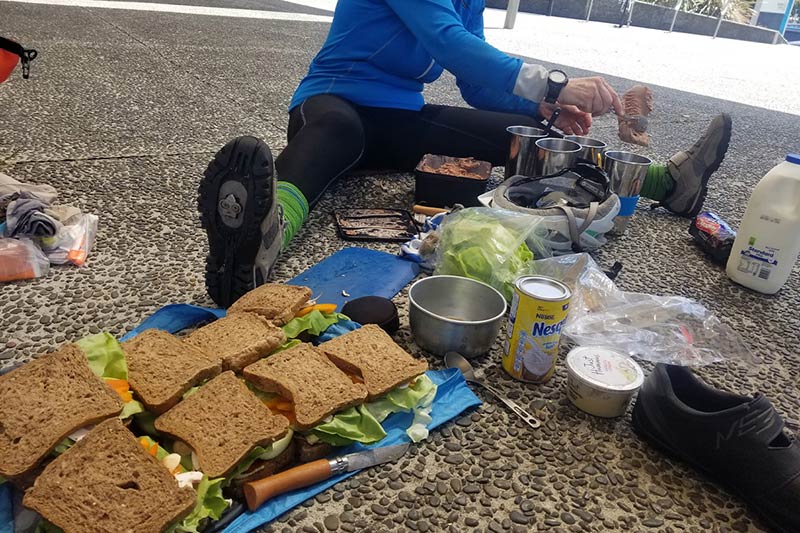 Cyclist sitting on ground preparing food and sandwiches for several people
