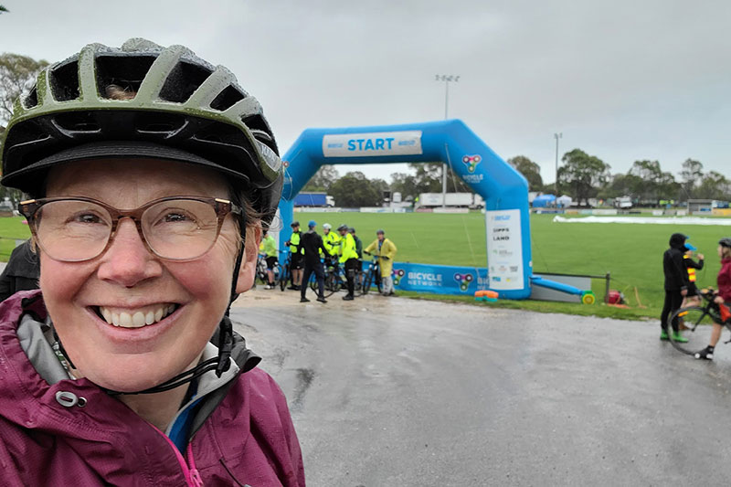 Monica smiling wearing bike helmet near start line of bike race